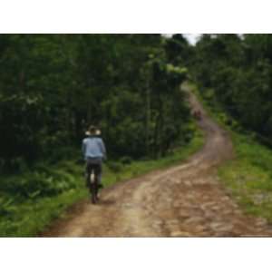  A Man on a Bicycle Pedals Down a Dirt Road Through a Rural 